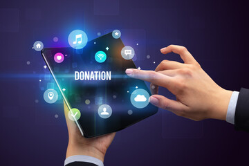 Businessman holding a foldable smartphone with DONATION inscription, social media concept
