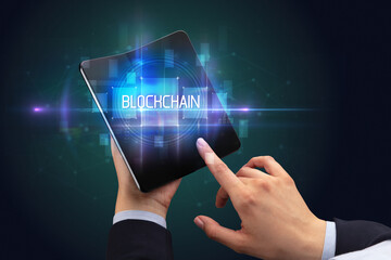 Businessman holding a foldable smartphone with BLOCKCHAIN inscription, new technology concept