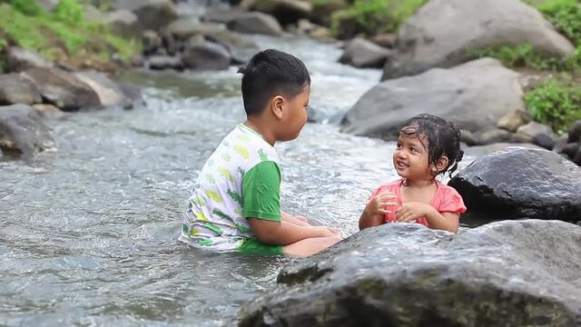 Two asian children playing water in the river in a mountainous area