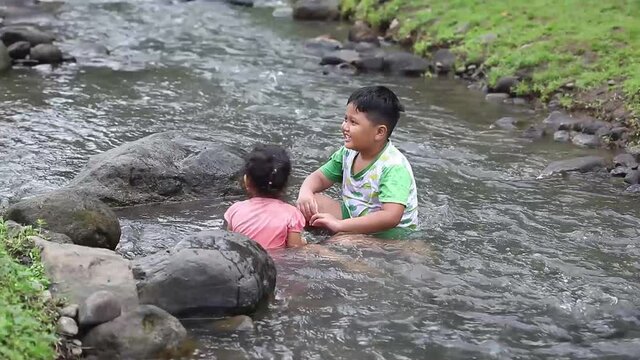 Two asian children playing water in the river in a mountainous area