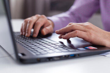 Male executive hands typing and scrolling on a laptop computer device with blur background. Working online from home. 
