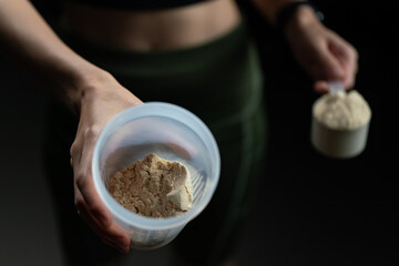 Close up of women with measuring scoop of whey protein, jar and shaker bottle, preparing protein...