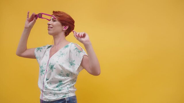 Funny Red Hair Woman With Pink Sunglasses Dancing Over The Yellow Background. Woman In Her 40s