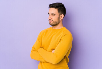 Young caucasian man isolated on purple background suspicious, uncertain, examining you.