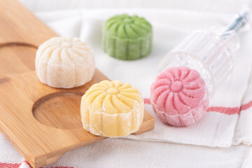 Obraz na płótnie Canvas Colorful snow skin moon cake, sweet snowy mooncake, traditional savory dessert for Mid-Autumn Festival on bright wooden background, close up, lifestyle.