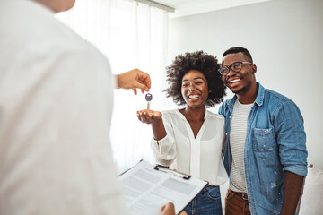 Happy couple is taking keys from their new house from broker and smiling. Hands of estate agent...
