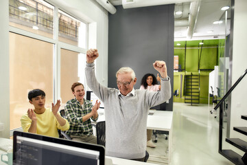Aged man, senior intern looking cheerful, raising his arms after completing first task at work, Friendly workers applauding, cheering new employee in the office