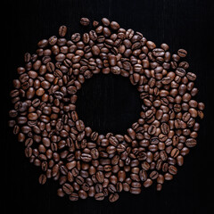 Circle frame of roasted brown coffee beans on wooden background.