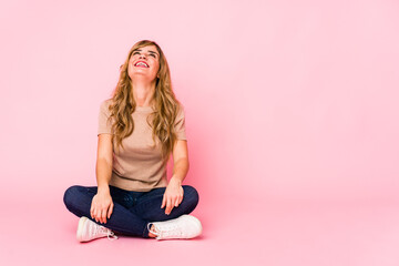 Young blonde caucasian woman sitting on a pink studio relaxed and happy laughing, neck stretched showing teeth.