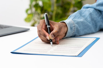 Close-up of a man hand writing or signing in a document on a desk at home or office