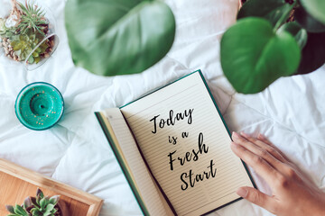 Woman holding a diary with inscription today is a fresh start with plants and succulents on white...
