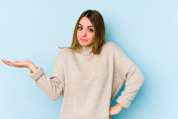 Young caucasian woman isolated on blue background doubting and shrugging shoulders in questioning...