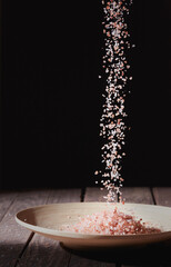 Pouring Himalayan salt over a bamboo bowl, on a wooden table. All on a dark background