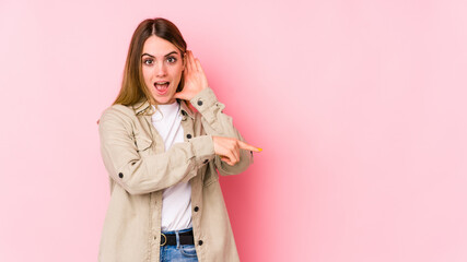 Young caucasian woman isolated on pink background trying to listening a gossip.