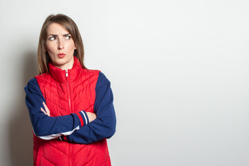 Young woman with a serious face looks to the side in a red vest on a light background