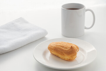 The custard eclair cake lies on a white plate with a glass on the background. Photography in a light key