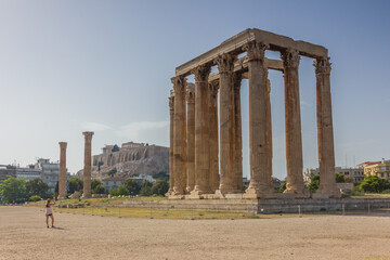 Tourist taken a photo to the Greek ruins of the Temple of Olympian Zeus in Athens with the Acropolis in the back in a sunny summer day with blue sky.