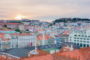 Fototapeta na wymiar View of beautiful and colourful houses from above during sunrise with orange and pink sky in Lisbon, Portugal.