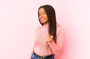 Young african american woman isolated on a pink background pointing with finger at you as if inviting come closer.