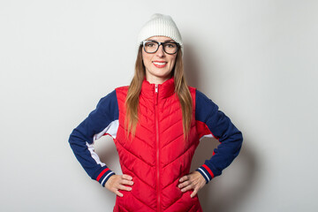 Fototapeta premium Young woman with a smile in a red vest, hat and glasses on a light background