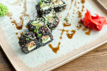 Set of rolls of black rice, fish and philadelphia cream cheese, sesame seeds, on a white plate, poured with unagi sauce and microgreen sprouts, top view