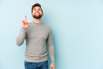 Young caucasian man isolated on blue background indicates with both fore fingers up showing a blank...