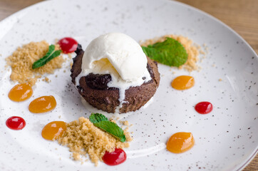 Delicious sweet chocolate fondant with drops of colorful jam and a scoop of melted ice cream, on a white plate in a cafe