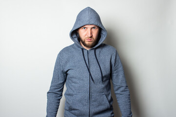 Young man in a hood with a serious, aggressive face on a light background