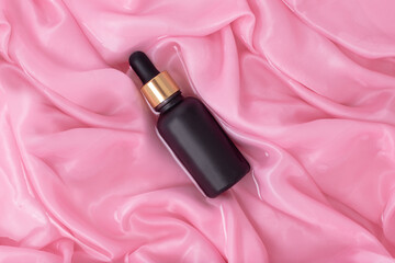 Matte black cosmetic bottle with dropper on a background of wet folds of pink silk. Mockup bottle for oil or essence.