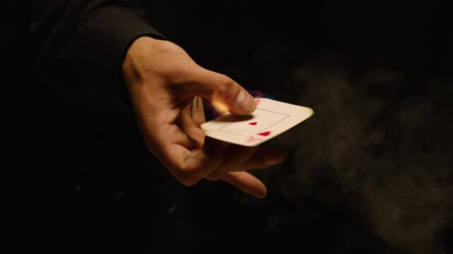 Close-up of a Magician Hand Performing Card Trick . Burning card on black Background with smoke . Card Mechanic rotating flaming jack card in hand . Shot on ARRI Alexa cinema camera in Slow Motion