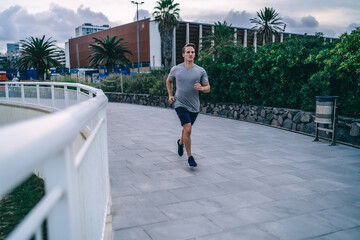 Handsome caucasian male runner in activewear having morning workout on urban settings reaching goals, determined sportsman running on cardio training in city prepare body shape for marathon