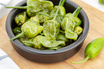 Close up of Cooked Padron peppers in a a bowl on wooden table. Traditional Spanish appetizer