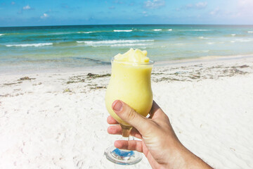 Pineapple cocktail on beach. Exotic holiday alcohol relaxation. Hand holding a glass full of mixed fruit.