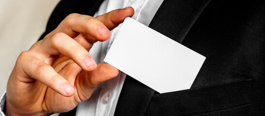 Obraz premium Part of body of man who takes out business card from the pocket of business suit, copyspace. Businessman in black business suit puts white card in pocket. Business concept.