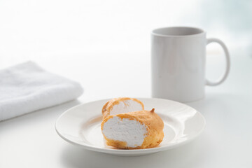 The custard cut eclair cake lies on a white plate with a glass on the background. Photography in a light key