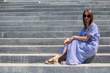 Fototapeta na wymiar Young woman in dress sits on steps in the park