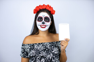 Woman wearing day of the dead costume over isolated white background smiling and showing blank notebook in her hand