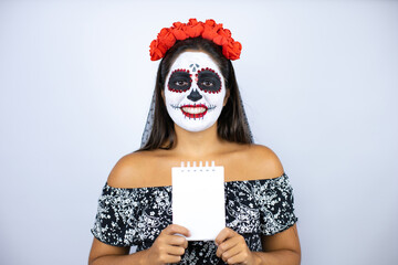 Woman wearing day of the dead costume over isolated white background smiling and showing blank notebook in her hand