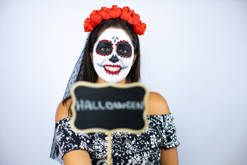 Woman wearing day of the dead costume over isolated white background smiling and holding blackboard with halloween word message