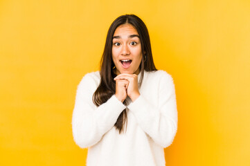Young woman isolated on a yellow background praying for luck, amazed and opening mouth looking to front.
