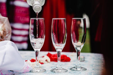 Man hands pouring champagne from a bottle in glass that stand on table. Close up. The man fills the glasses elite drinks.