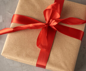 knotted bow made of red silk ribbon on brown kraft paper background