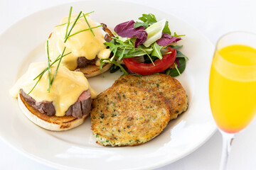 Eggs Benedict with beef asparagus and roasted tomato. Brunch on white table. Eggs benedict salad and mimosa cocktail