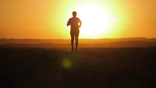 Running man silhouette in sunset time. Outdoor cross-country running. Athletic young man is running in the nature during golden sunset. Healthy lifestyle.