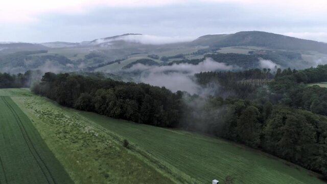 Dramatic, moody field and forrest covered in fog with mountains in the background