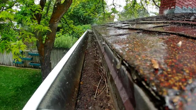 Rain water is seen pouring down shingles and a rain gutter in slow motion.