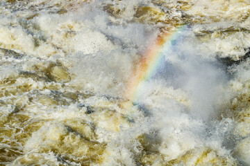 Fototapeta na wymiar Splashing water waves with rainbow on the fast river