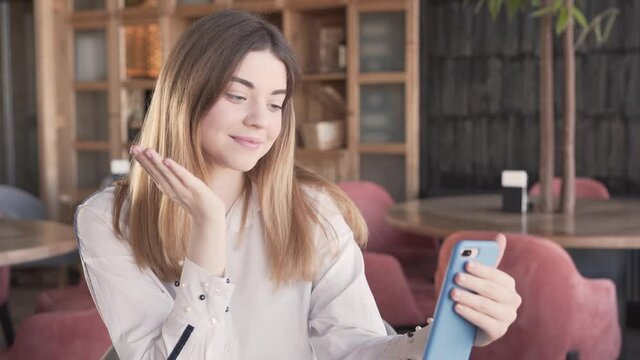 A sweet young girl does a video call via her phone. She poses, smiles a lot and sends air-kisses. The background is blurred.