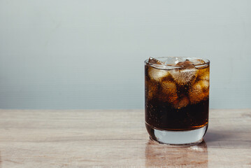 Cola and ice cube in clear glass on wooden table