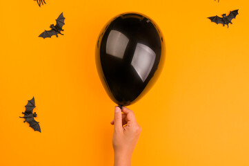  Bats and a black balloon in hand on an orange background. Halloween decor. Copy space. High quality photo